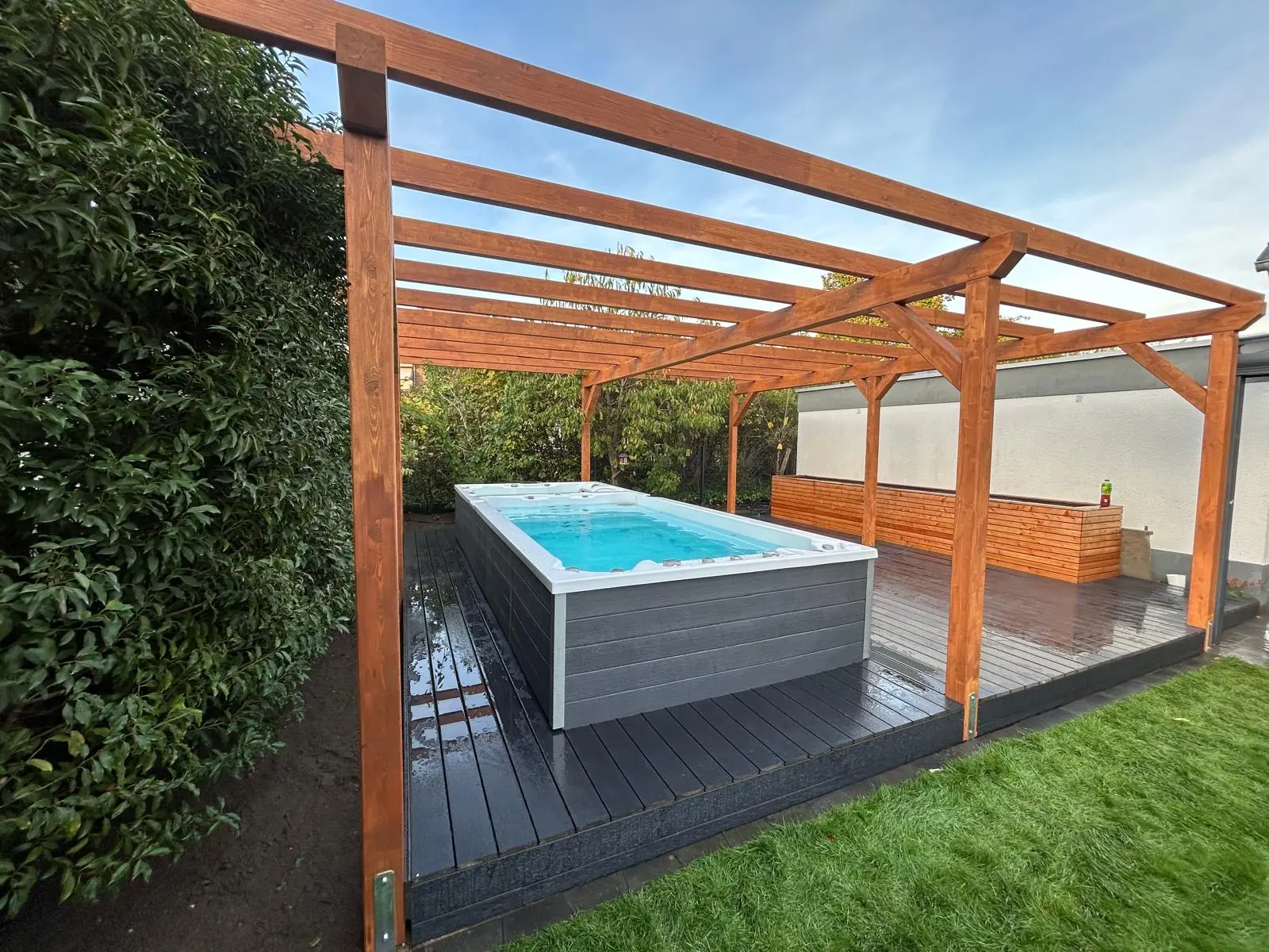 Swim spa INFINITAS seminterrata in un deck scuro sotto una pergola