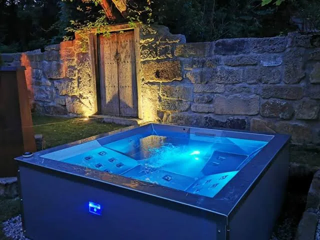 Minipiscina INFINITAS davanti a un muro in pietra con luce blu